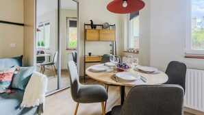 Uma área de refeições moderna com uma mesa redonda para quatro pessoas, um sofá com manta branca e uma luminária pendente vermelha.