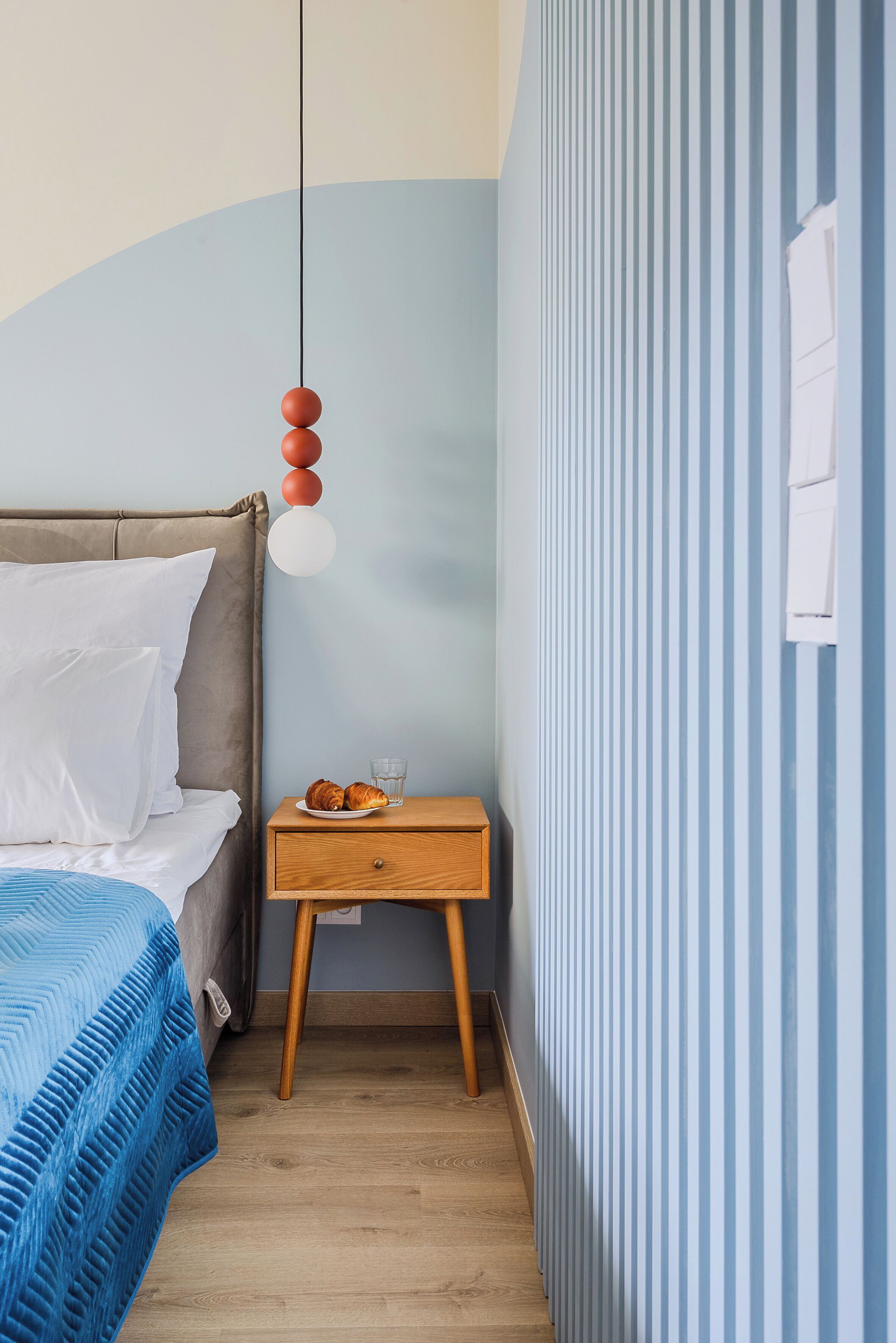 Une chambre à coucher avec un lit, une table de chevet et un mur orné de rayures verticales.