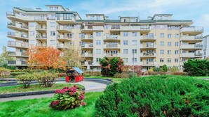 Um edifício residencial de vários andares com varandas, um pequeno jardim com um coreto e um gramado bem cuidado.