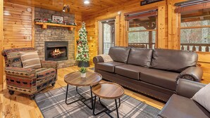 Una sala de estar acogedora con chimenea, un sofá de cuero, un sillón estampado y un árbol de Navidad.