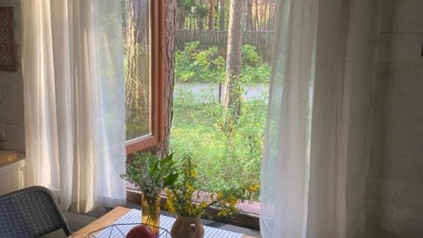 Una habitación con un ventanal grande, una silla y una mesa con un jarrón de flores.