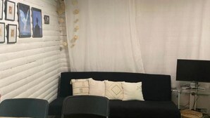 Una habitación con pared de madera blanca, un sofá negro, una mesa de comedor con sillas y cuadros en la pared.