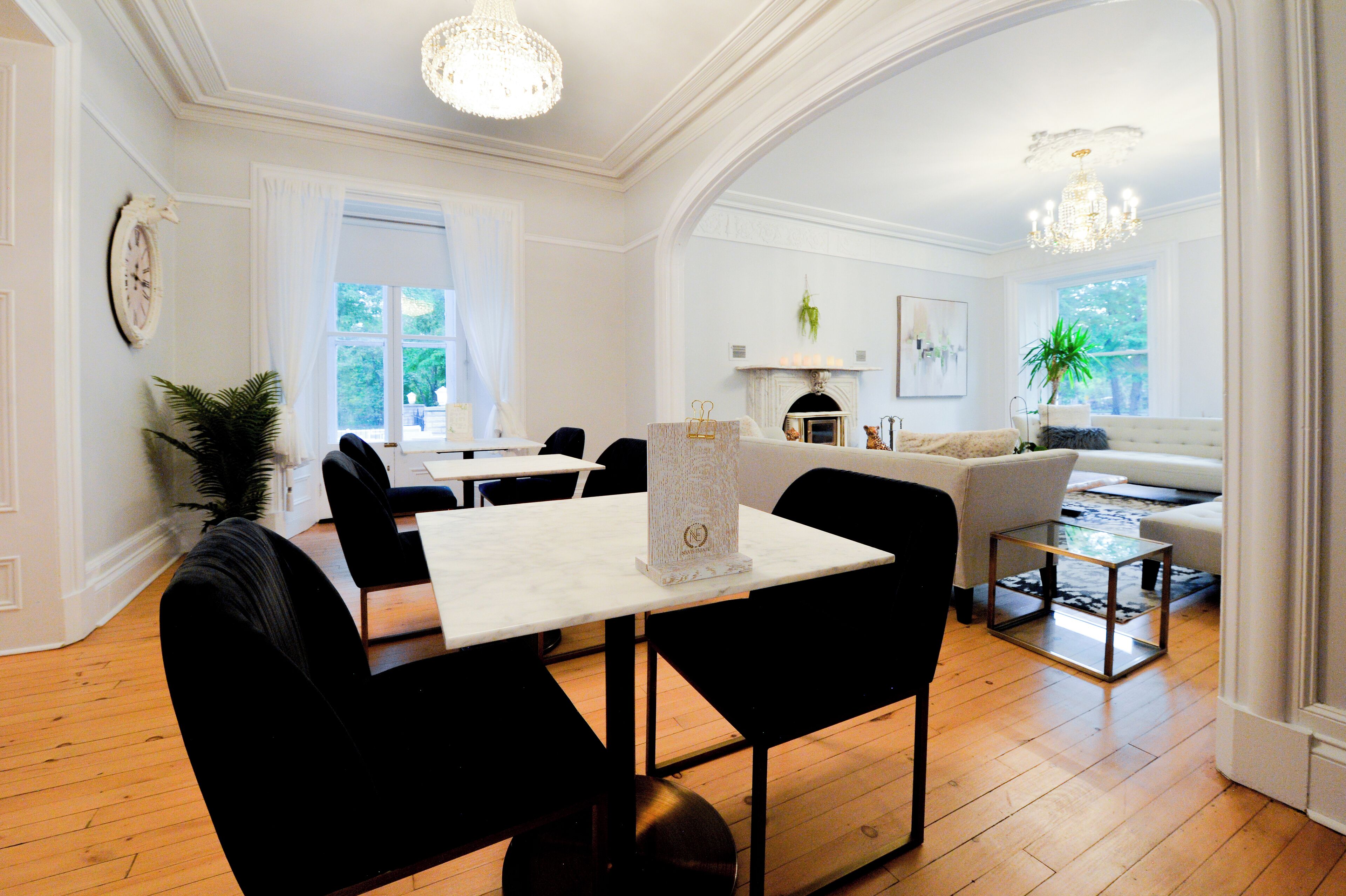 A dining area with a white table and black chairs, a chandelier, and a fireplace with a mantel.