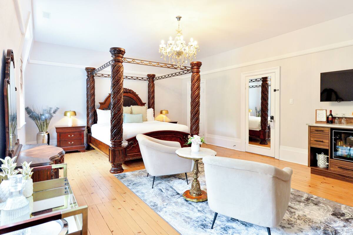 Un dormitorio con cama con dosel, un candelabro, un televisor y un comedor con mesa y sillas.