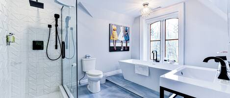 A modern bathroom with a glass shower enclosure, a white toilet, a bathtub, and a large vanity with a sink.