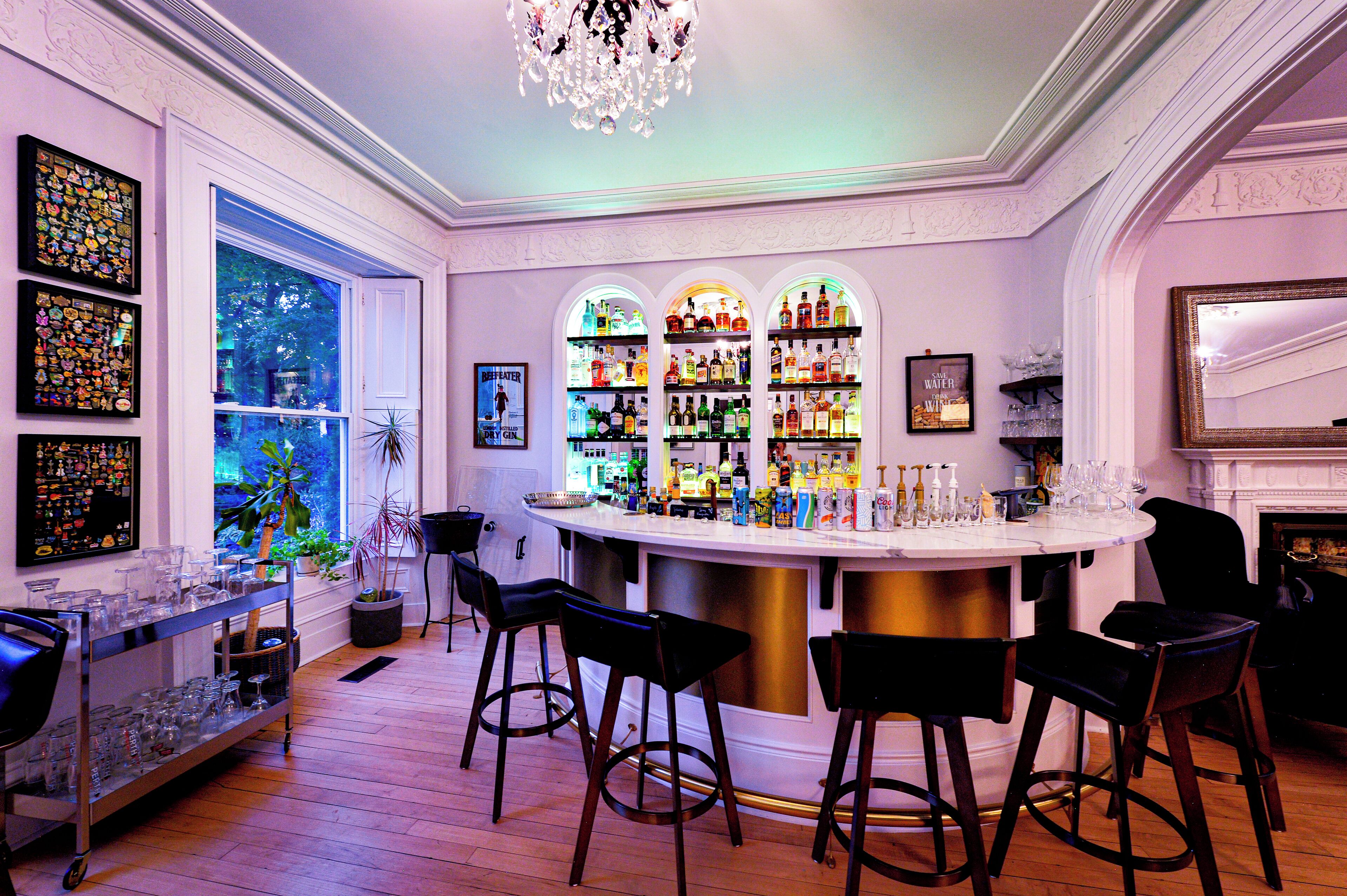 A bar area with a white countertop, multiple shelves of bottles, and black bar stools.