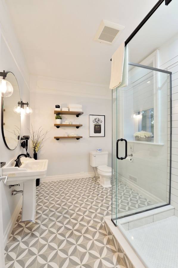 A modern bathroom with a geometric patterned floor, a glass shower enclosure, a white sink, and a toilet. - Nevis Estate Boutique Hotel (Perth)