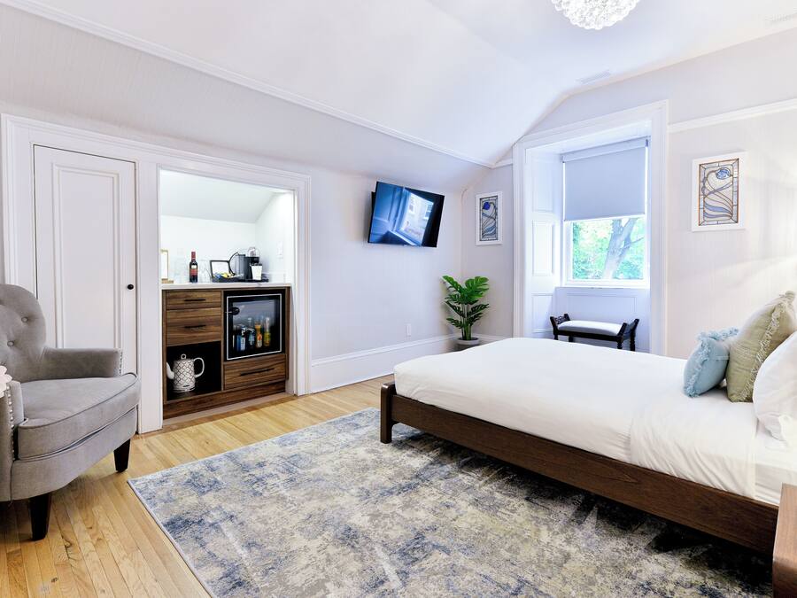 A bedroom with a bed, a chair, a TV, a plant, and a window.