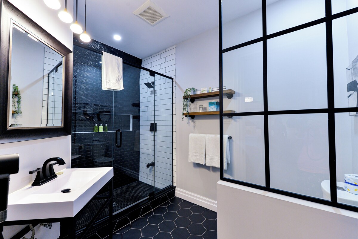 Un baño moderno con cabina de ducha de vidrio, un lavabo blanco y una repisa con artículos de aseo.