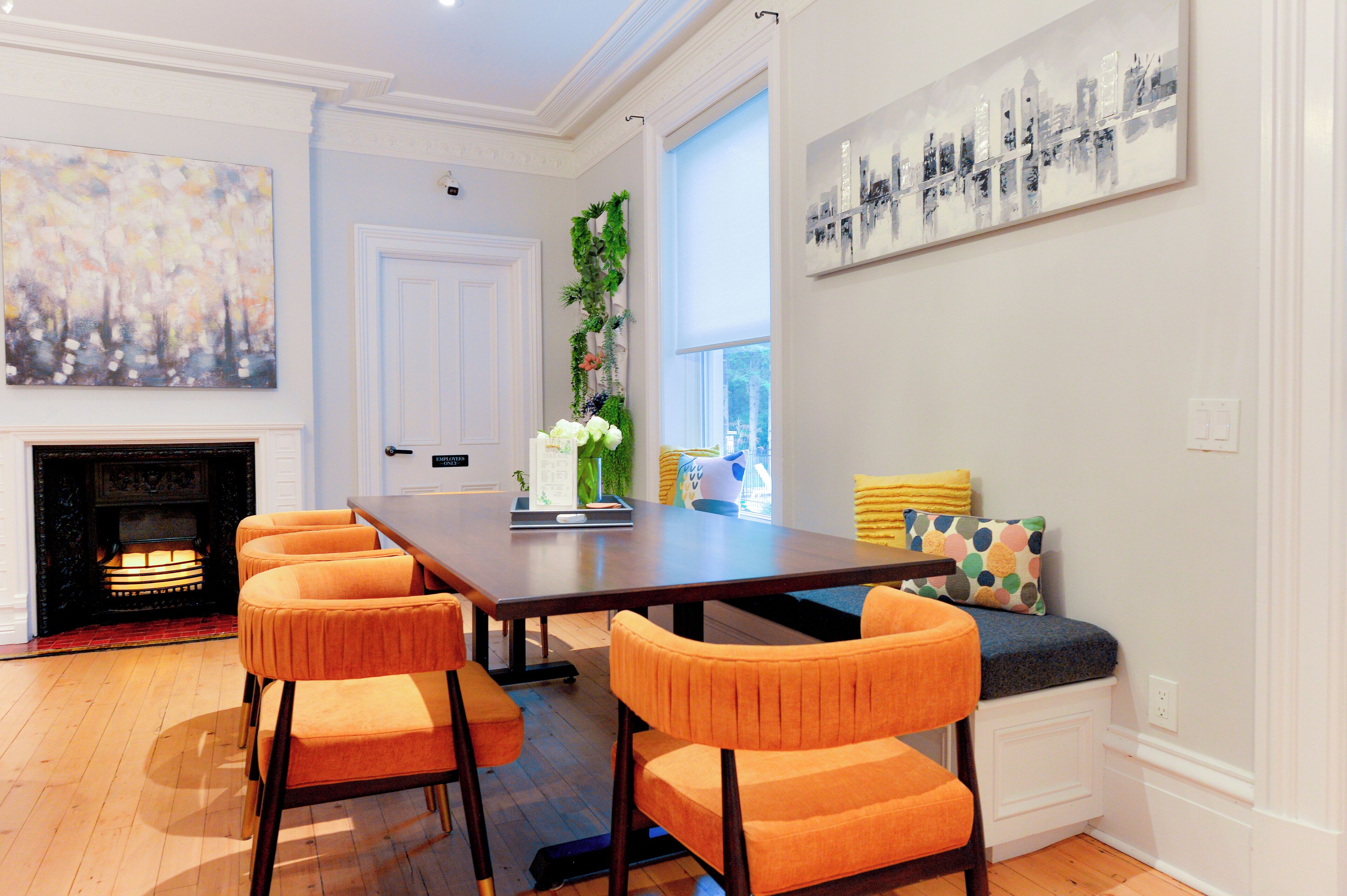 A dining area with a wooden table and orange chairs, a fireplace, and artwork on the walls.