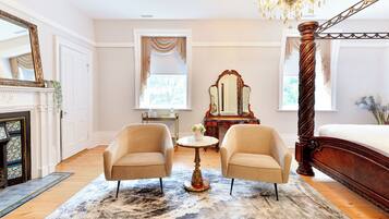 A bedroom with a large bed, two armchairs, a round table, a mirror, and a chandelier.