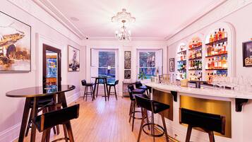 Una zona de bar con suelo de madera, taburetes, una barra con botellas y cuadros en las paredes.