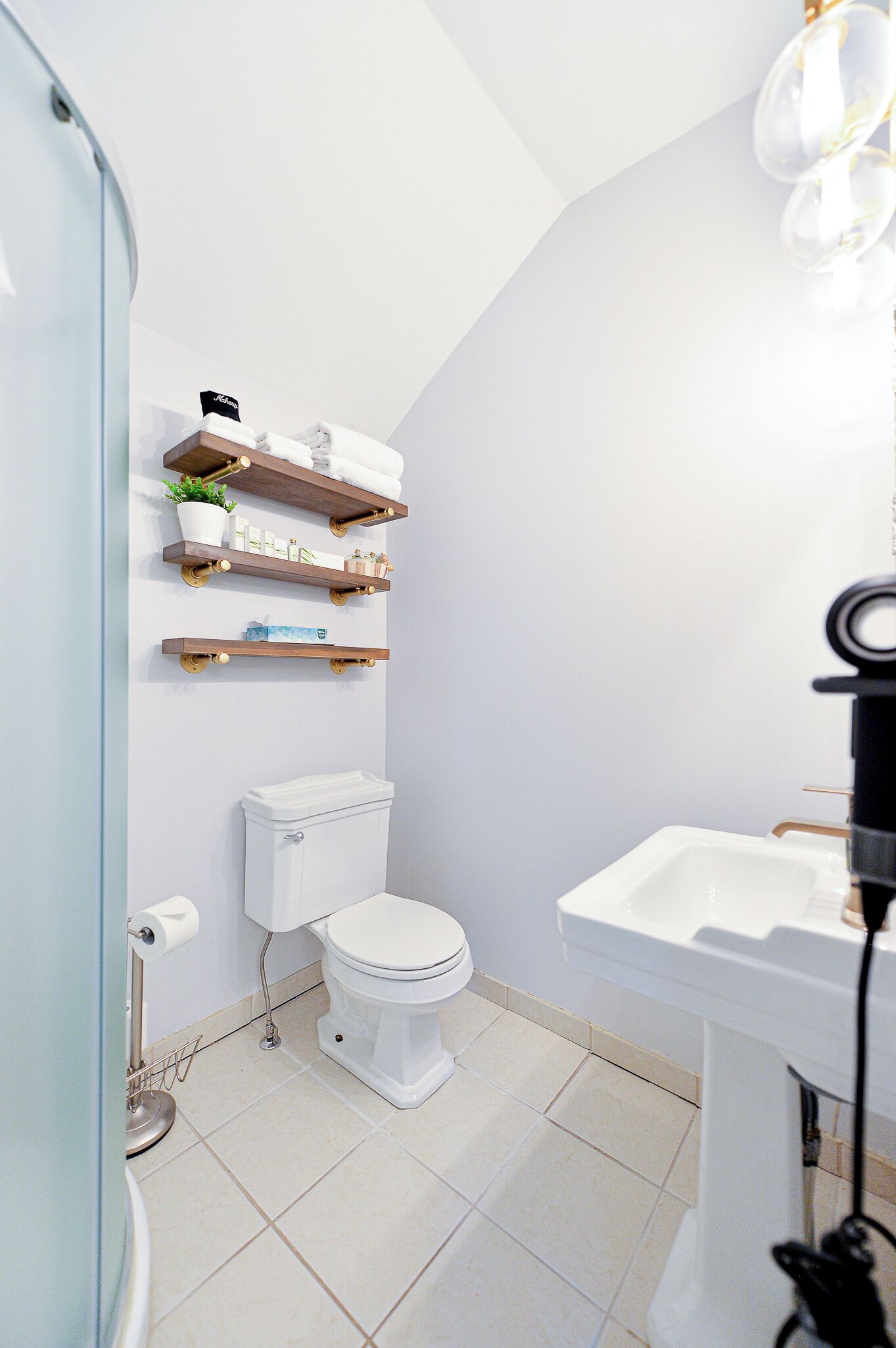 A bathroom with a toilet, white sink, and shelves with toiletries.