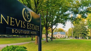 A sign for Nevis Estate Boutique Hotel with a well-maintained lawn and a large house in the background. - Nevis Estate Boutique Hotel (Perth)