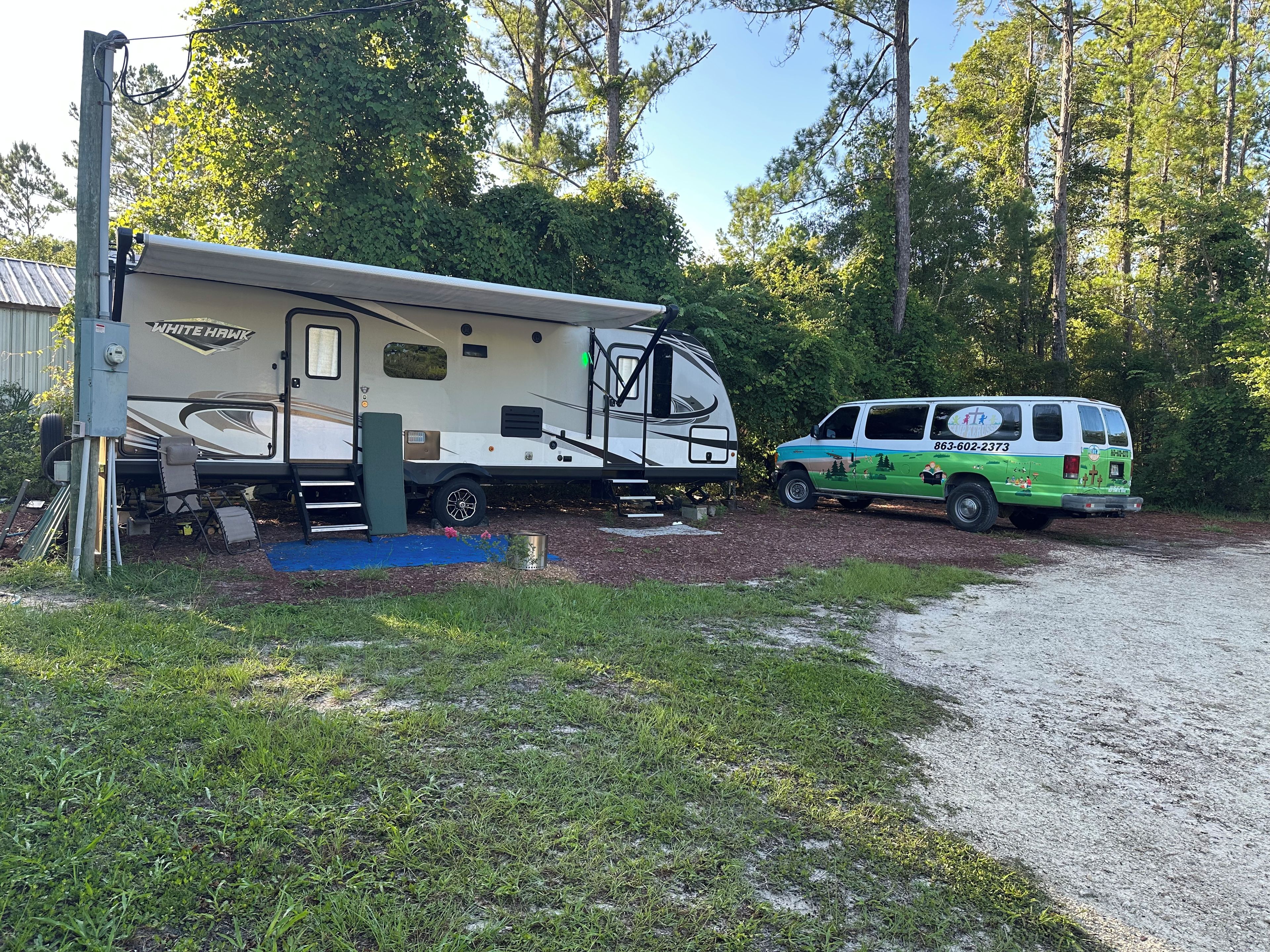 A recreational vehicle (RV) and a service van parked on a gravel path with a blue mat in front.