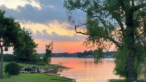 Uitzicht op een meer met een houten steiger die uitkomt op een gazon, kano's en een zonsondergang.