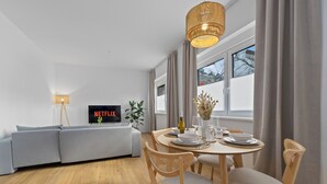 A modern living room with a grey sofa, a dining table set for four, and a TV displaying 'NETFLIX'. - Central | Modern | Old Town | Parking lot | 70 m² (Bad Kreuznach)