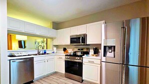 Una cocina moderna con armarios blancos, electrodomésticos de acero inoxidable y piso de madera en patrón de espiga.