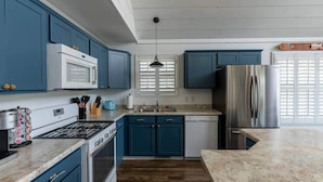 A modern kitchen with blue cabinets, stainless steel appliances, and a wooden floor. - Insta-worthy Rock River cabin (Byron)