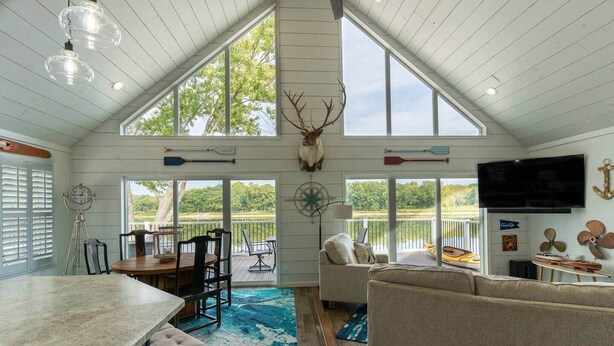 A spacious living room with a large window, a dining area with a wooden table, and a kitchen with a marble countertop. - Insta-worthy Rock River cabin (Byron)