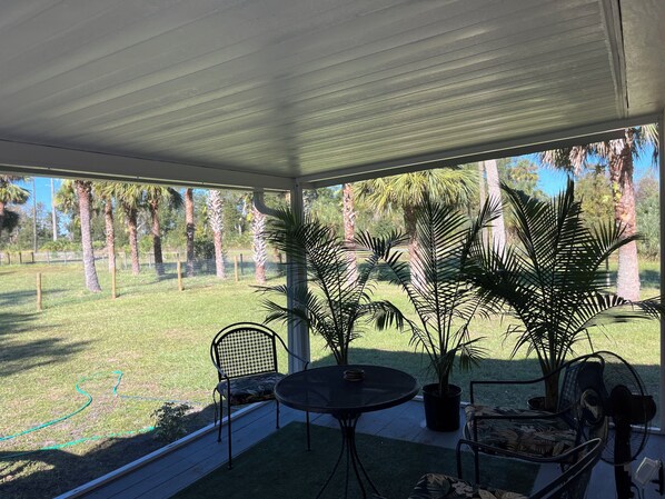 Une terrasse couverte, dotée d’une table et de chaises, qui donne sur une pelouse agrémentée de palmiers.