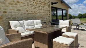 An outdoor seating area with wicker furniture and cushions, a glass-top table, and a stone wall backdrop.