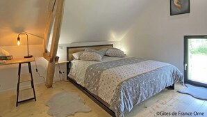 A bedroom with a sloped ceiling, a bed with patterned bedding, a desk with a lamp, and a framed artwork on the wall.