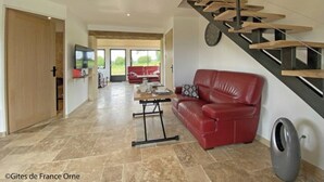 A spacious living area with a red leather sofa, a wooden staircase, and a large window offering a view of the outdoors.