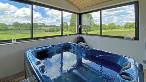 A hot tub in a room with large windows overlooking a green landscape.