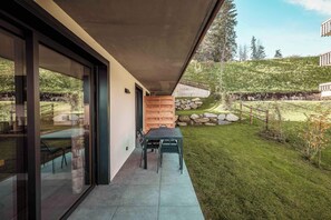 A modern house with a covered patio, a stone wall, and a grassy yard. - Apartment Nid des Neiges - Perfect for families (Combloux)