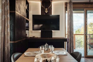 A dining area with a wooden table, chairs, and a television mounted on a dark wall. - Apartment Nid des Neiges - Perfect for families (Combloux)