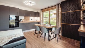 A modern kitchen with dark cabinets, a built-in oven, and a dining area with a wooden table and four chairs.