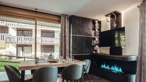 A modern living room with a fireplace, a dining area with chairs, and a TV mounted on a dark wall.