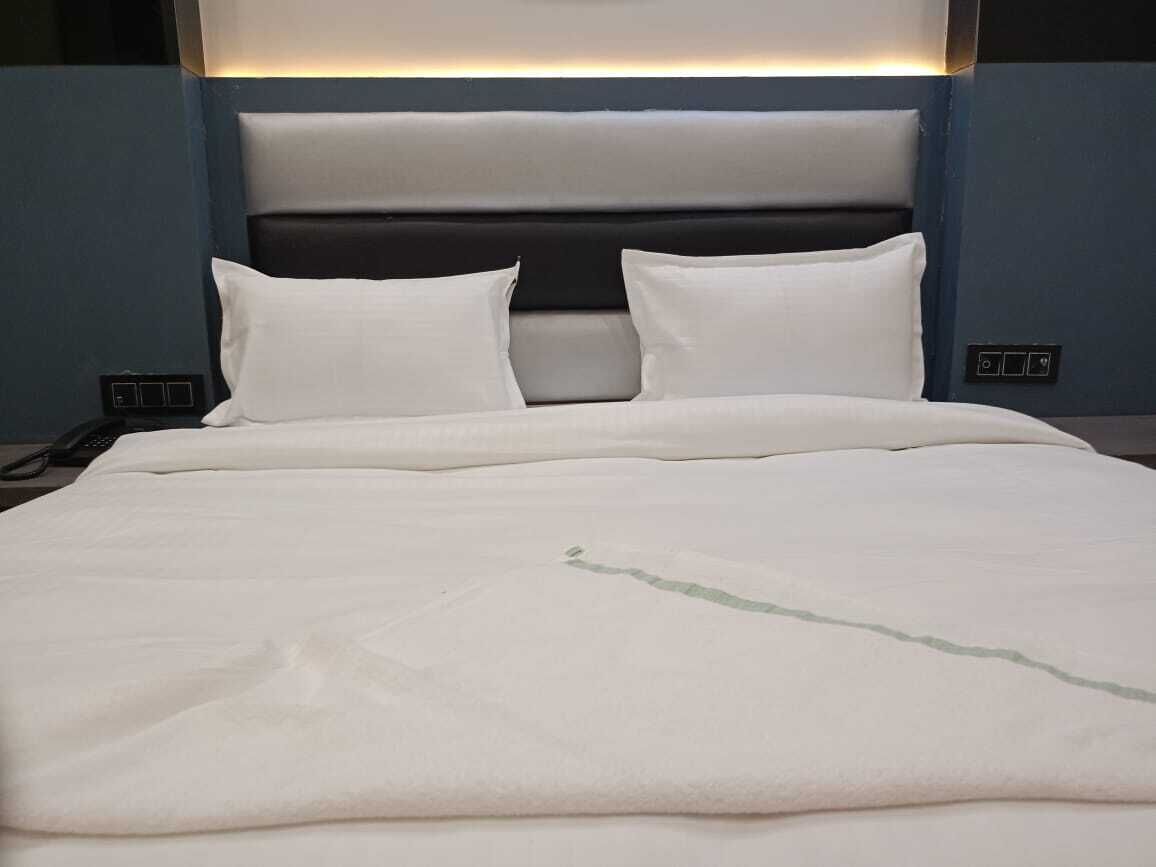 A neatly made bed with white bedding and a headboard with a lighted panel.