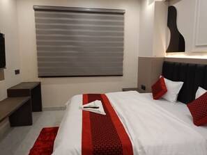 Ein Hotelzimmer mit einem Bett, einer rot-weißen Tagesdecke, einem roten Zierkissen, einem grauen Fensterrollo, einem schwarzen Kopfteil, einer Wanddekoration in Form einer Gitarre und einem roten Teppich.