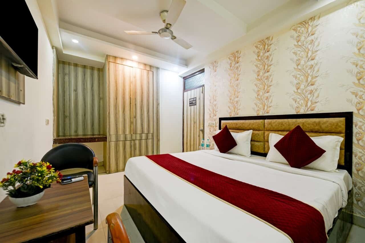 A hotel room with a bed, a desk with a chair, a ceiling fan, and a window with curtains.