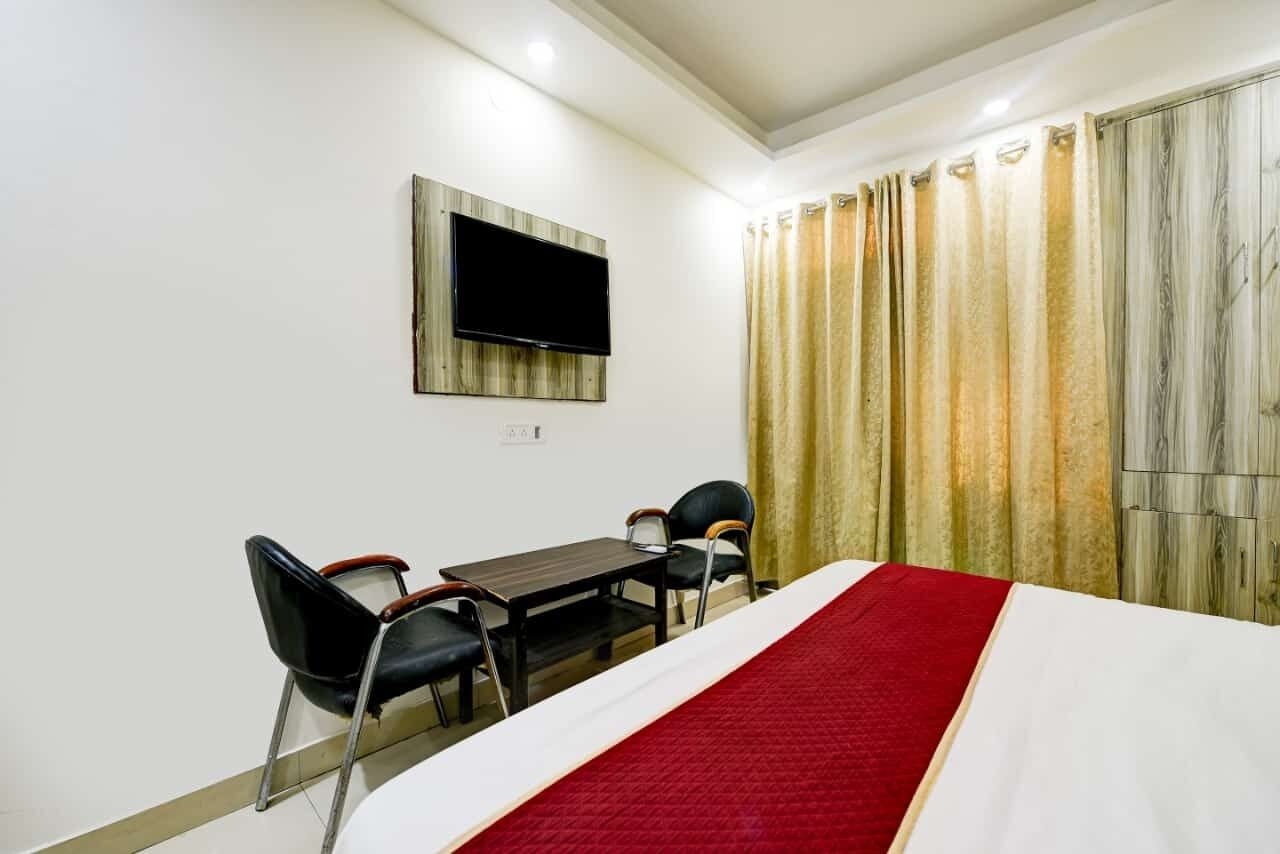 A hotel room with a bed, a TV mounted on the wall, a desk with two chairs, and a window with curtains.