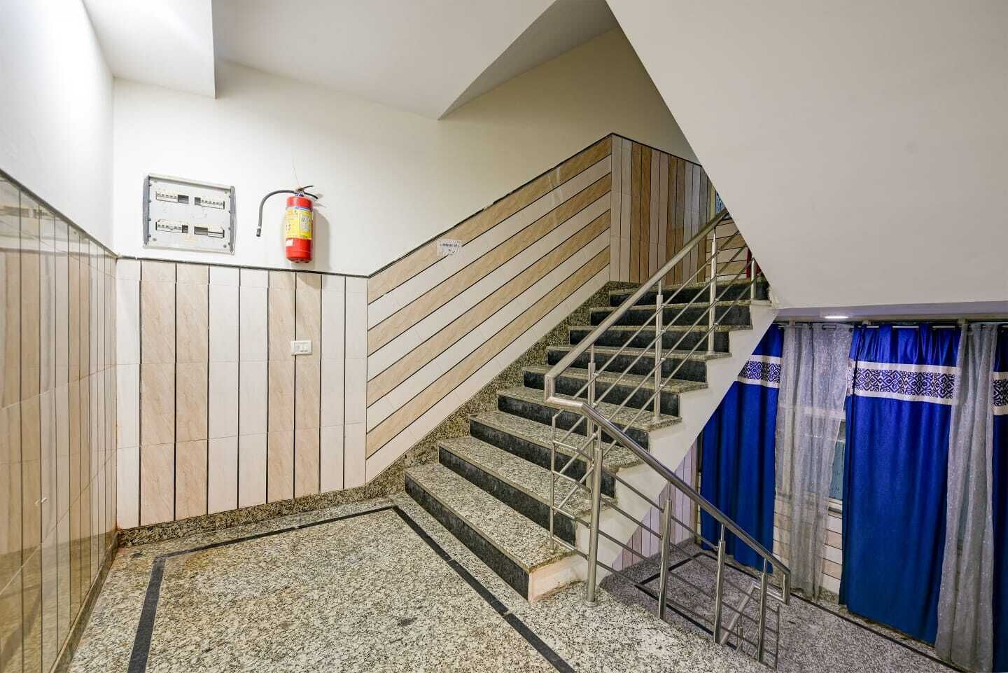 A staircase with a handrail, a fire extinguisher, and a blue curtain.
