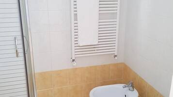 Ein Badezimmer mit Duschkabine aus Glas, Toilette in Weiß, Bidet und Handtuchhalter.