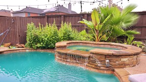 A backyard with a swimming pool, a stone waterfall feature, and a wooden fence. - Luxurious Retreat:Heated Pool, Hot Tub Media R, Minutes from Universal Kids Park (Frisco)