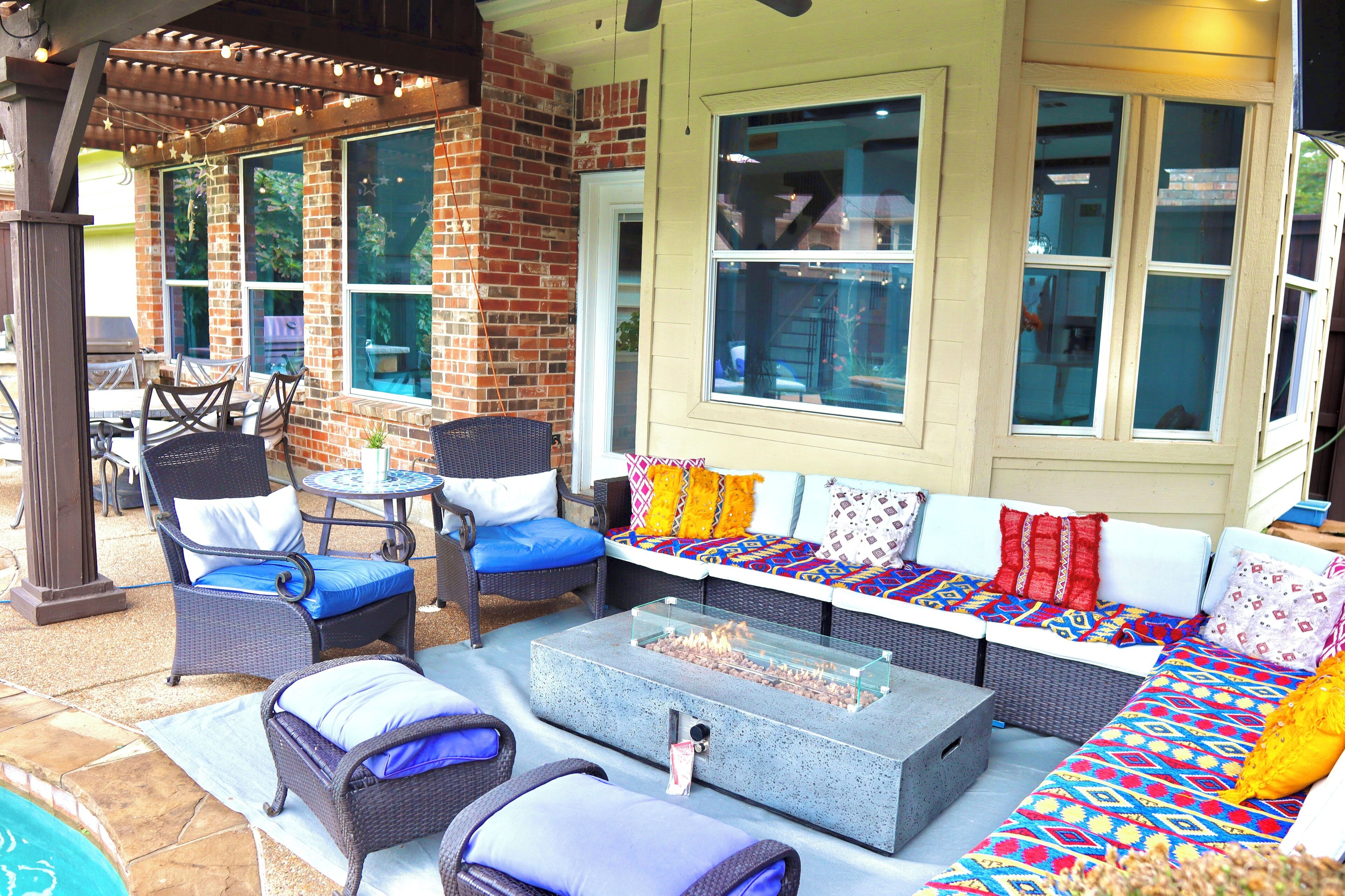 An outdoor patio area with wicker furniture, a fire pit, and large windows.