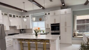A modern kitchen with white cabinetry, a large island with bar stools, stainless steel appliances, and a view of the outdoors. - Luxurious Retreat:Heated Pool, Hot Tub Media R, Minutes from Universal Kids Park (Frisco)