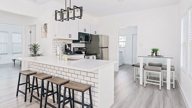 A modern kitchen with white cabinetry, a central island with stools, and a dining area with a glass table and chairs.