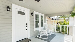 A porch with a white door, white rocking chairs, and a ceiling fan.