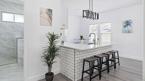 A modern kitchen with a white island, black bar stools, and a hanging light fixture.