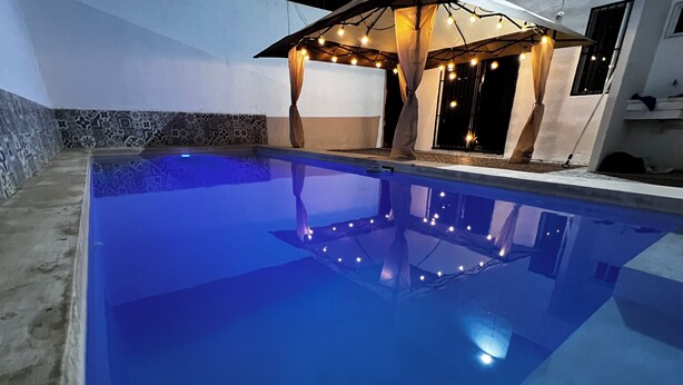 A swimming pool with a clear blue water surface, surrounded by a tiled wall and a stone border.