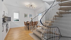 A modern kitchen with white cabinets, a dining area with a table and chairs, and a spiral staircase with a metal railing. - Maisonette | Old Town | Parking lot | 96 m² | Modern (Bad Kreuznach)