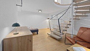 A modern interior with a wooden desk, a leather sofa, a spiral staircase, and a bed. - Maisonette | Old Town | Parking lot | 96 m² | Modern (Bad Kreuznach)