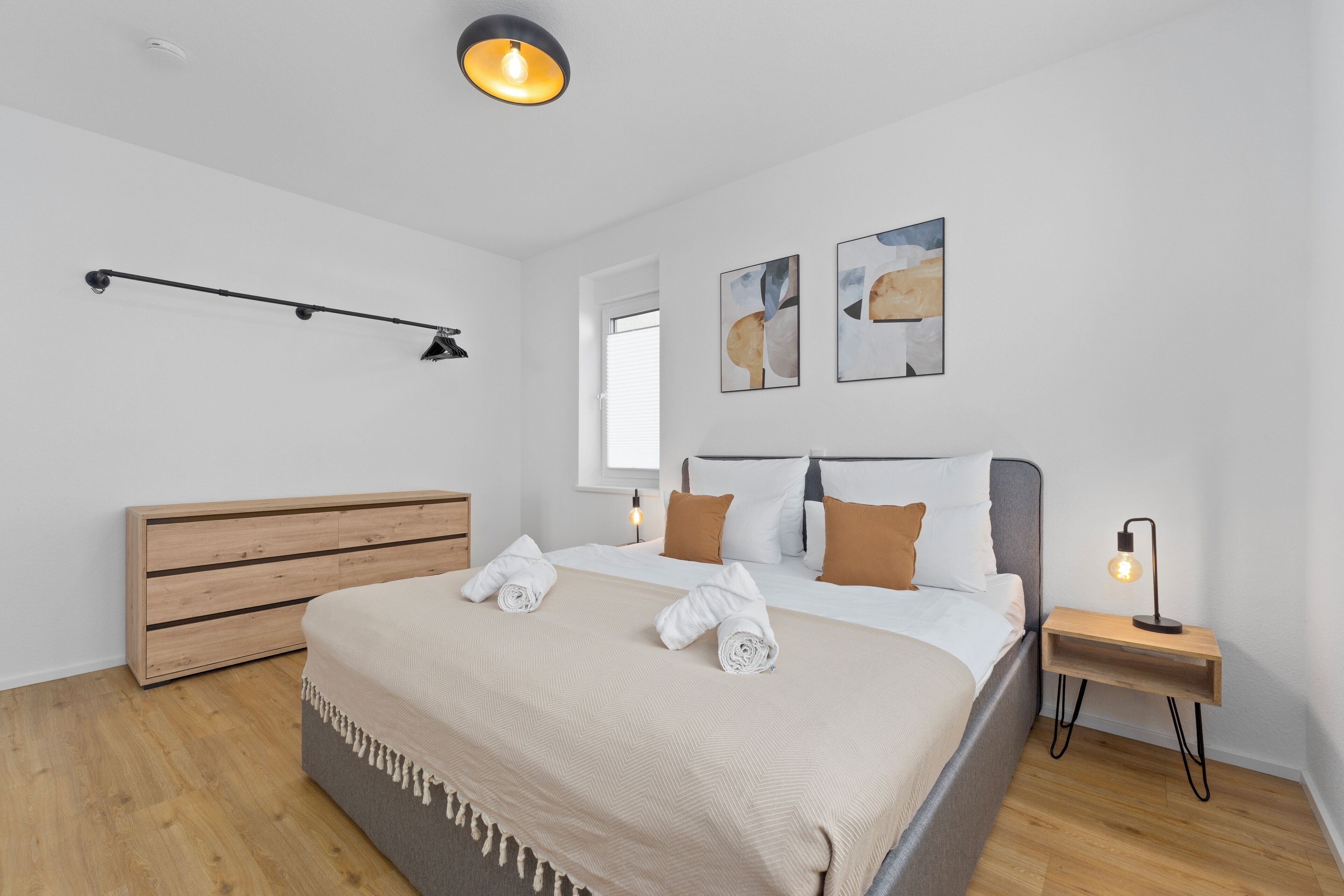 Une chambre moderne avec un lit en bois, une table de chevet avec une lampe et des œuvres d’art abstraites accrochées au mur.