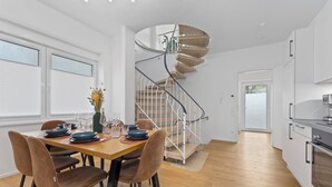 A modern kitchen with white cabinets, a wooden floor, and a spiral staircase. - Maisonette | Old Town | Parking lot | 96 m² | Modern (Bad Kreuznach)